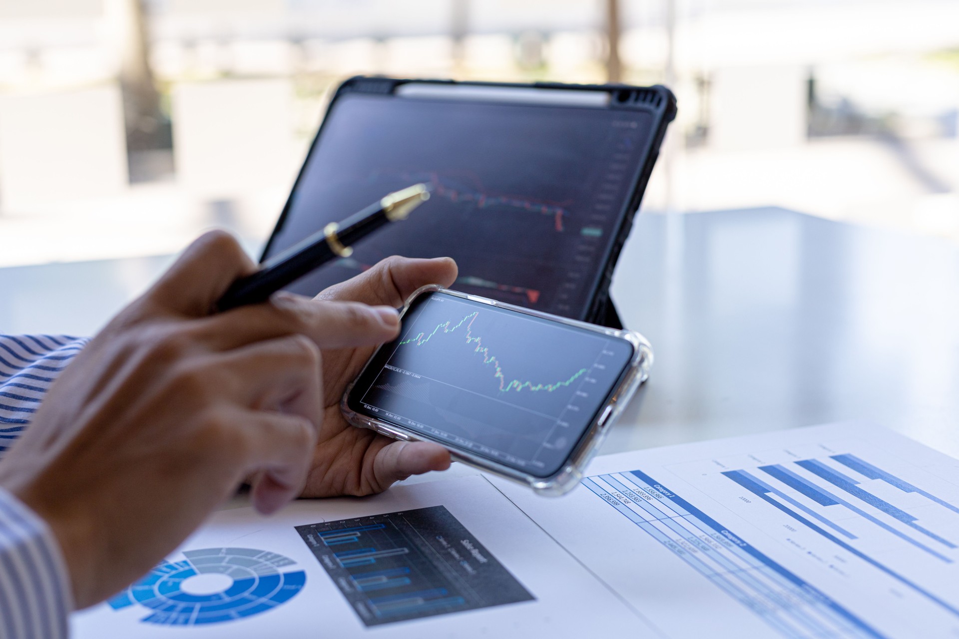 An investor is looking at stock charts on mobile phones and tablets, he is a stock investor, he trades stocks by analyzing the charts and using indicators to enter trades. Stock investment idea.